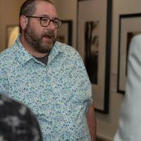 Man in flowery collared shirt talks with man in suit